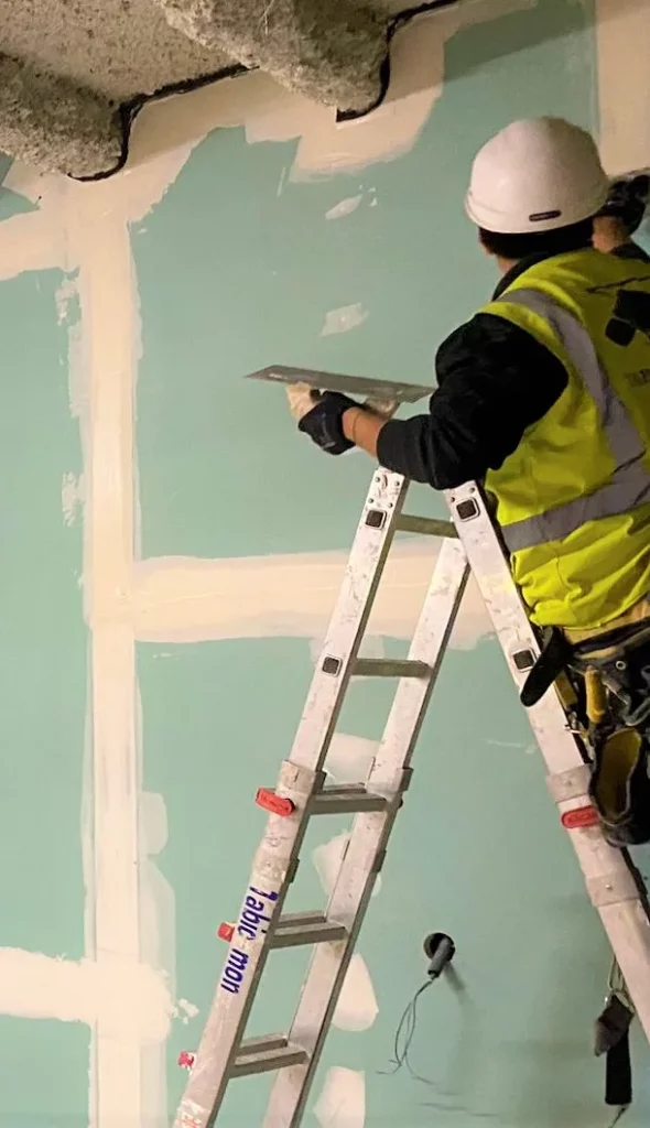 Trabajador de Tabic-Mon en una escalera instalando sistemas acústicos con habilidad y dedicación.